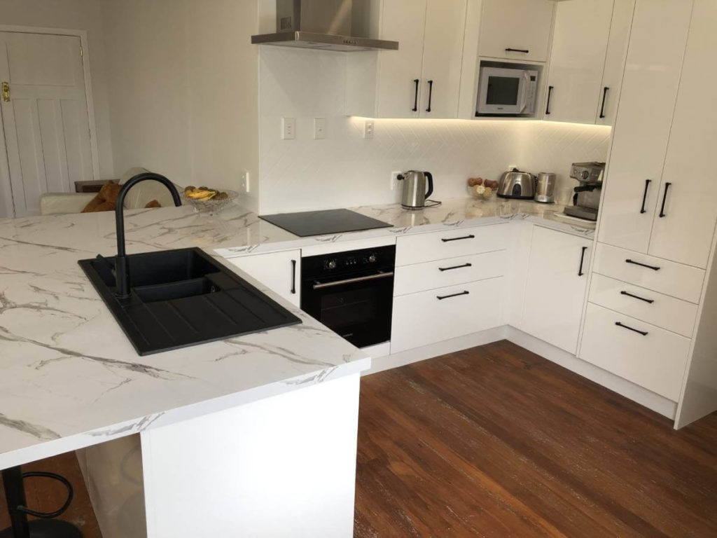 Renovated kitchen with stylish white cabinets and black appliances and sink